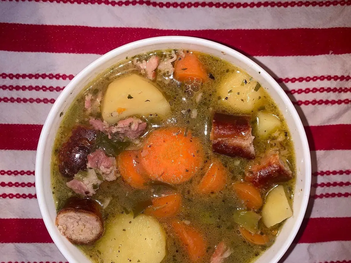 Cuenco de coddle con salchicha, bacon, patata, zanahoria y cebolla en caldo sobre un paño de rayas rojas