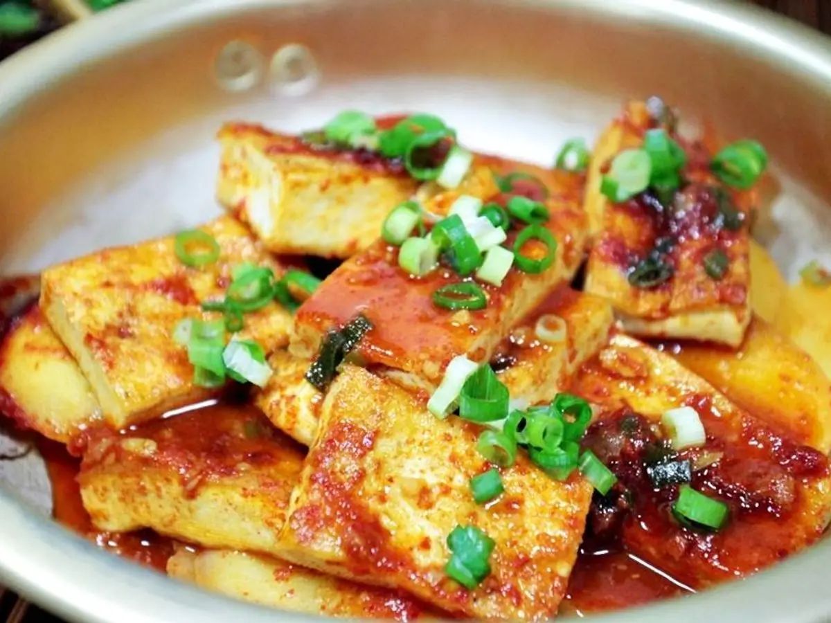 Tofu dorado en láminas glaseado con salsa picante y cebolleta picada en una sartén