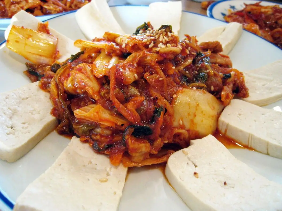 Kimchi salteado con cerdo en el centro rodeado de láminas de tofu templado en un plato blanco