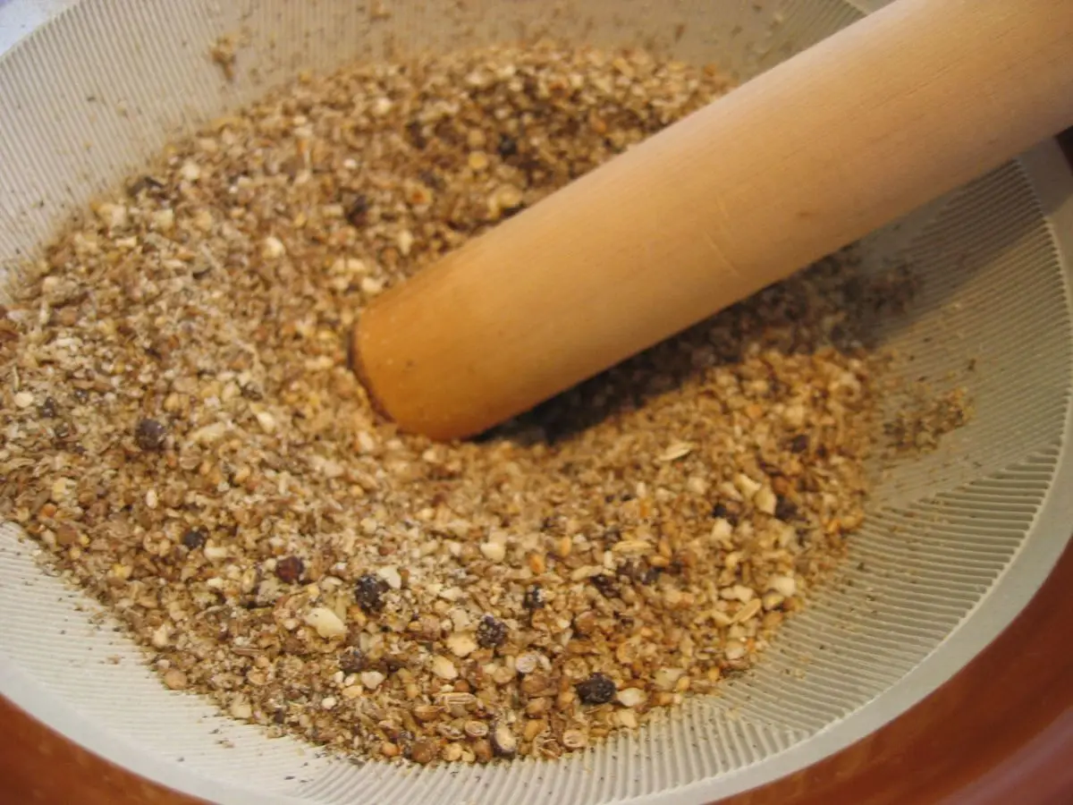 Mezcla de dukkah de frutos secos y especias machacados en un mortero de piedra con su mano de madera
