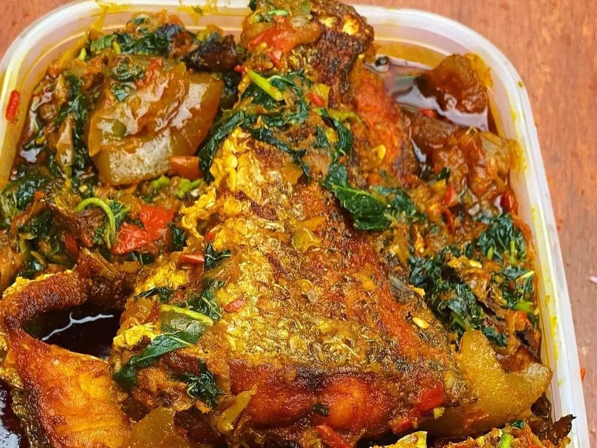 Guiso de verduras de hoja verde con pimiento y pescado frito entero en una fuente