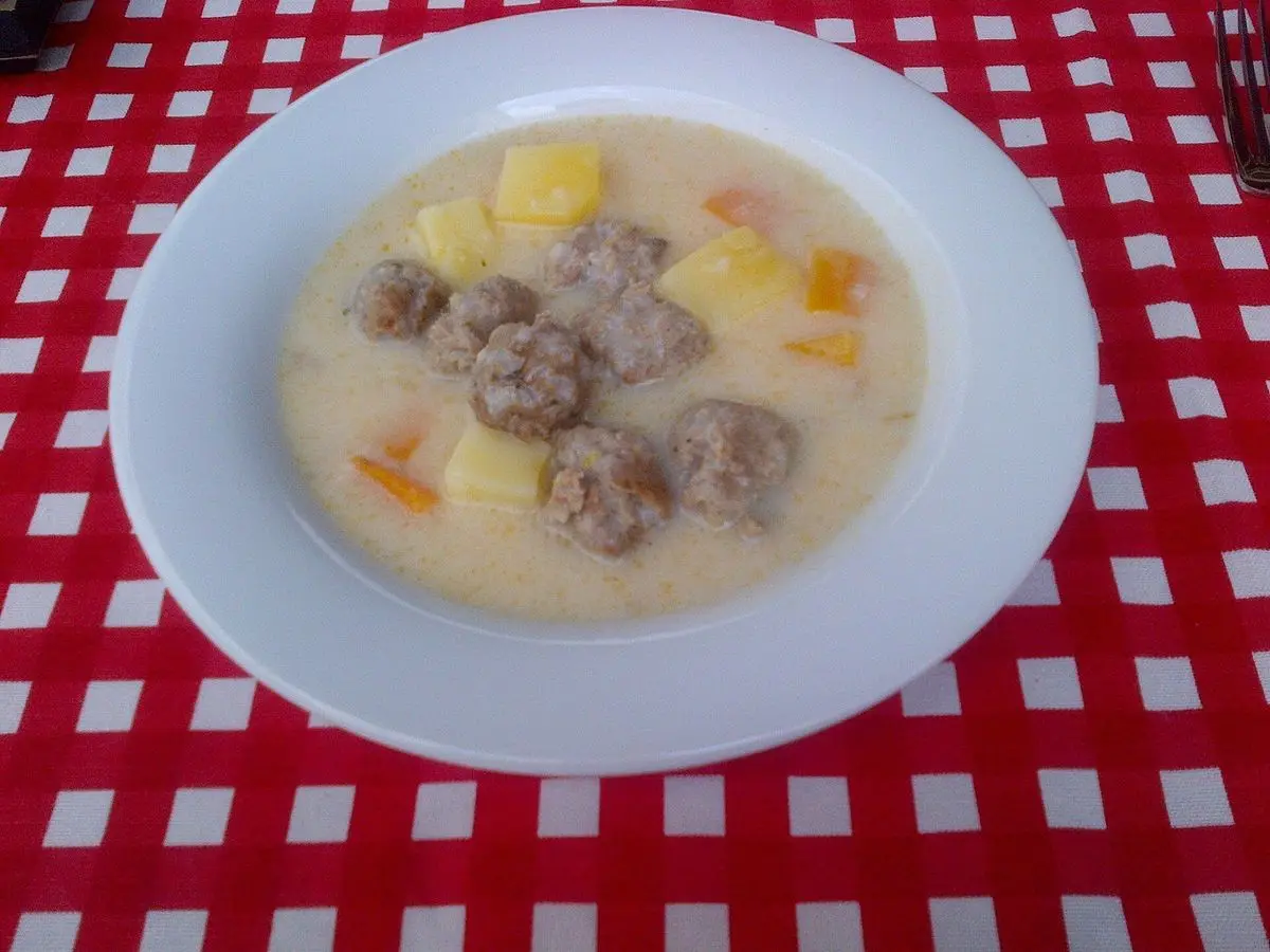 Plato hondo de sopa cremosa con albóndigas, patata y zanahoria sobre un mantel de cuadros rojos