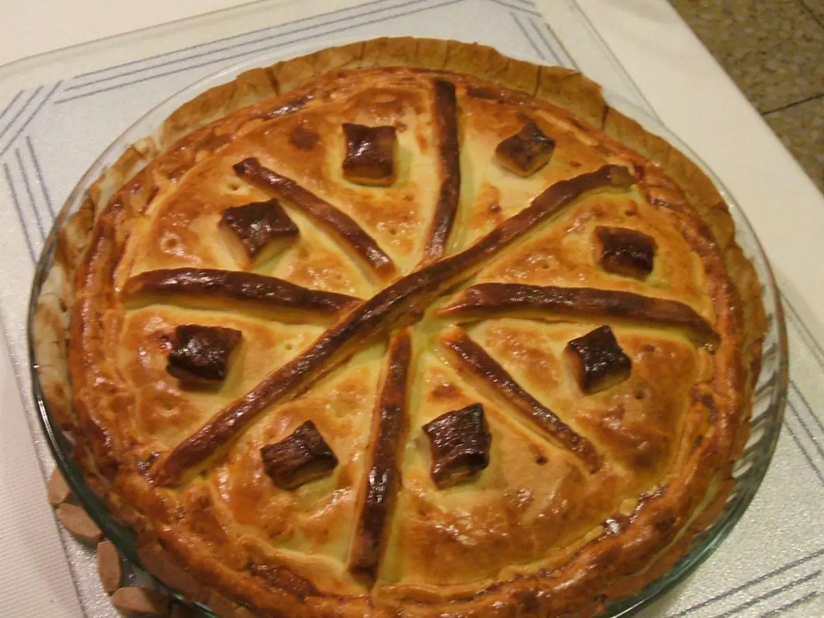 Empanada redonda dorada decorada con tiras de masa cruzadas en una fuente