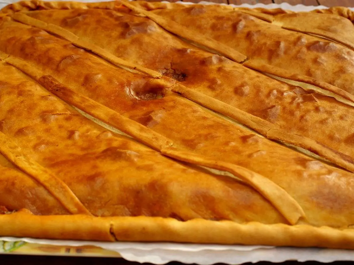 Empanada gallega entera de masa dorada cortada en porciones sobre papel