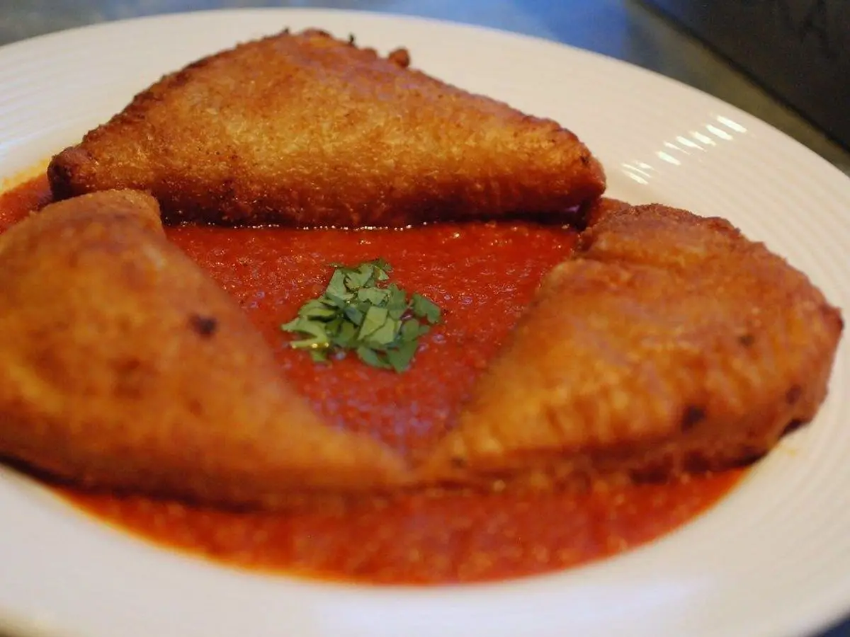 Dos empanadas fritas y doradas sobre salsa de tomate con una hoja de albahaca en un plato blanco
