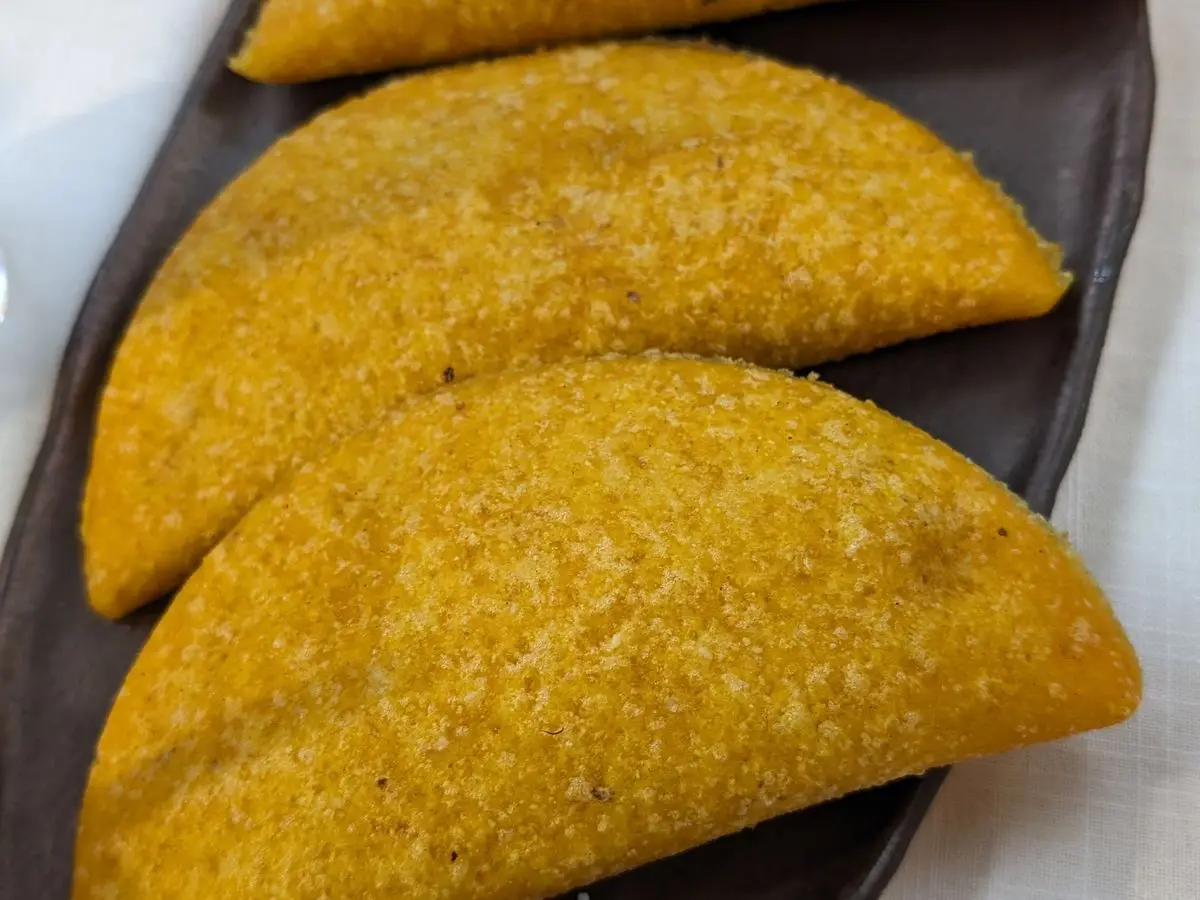 Dos empanadas doradas de masa de maíz en forma de media luna sobre una bandeja oscura