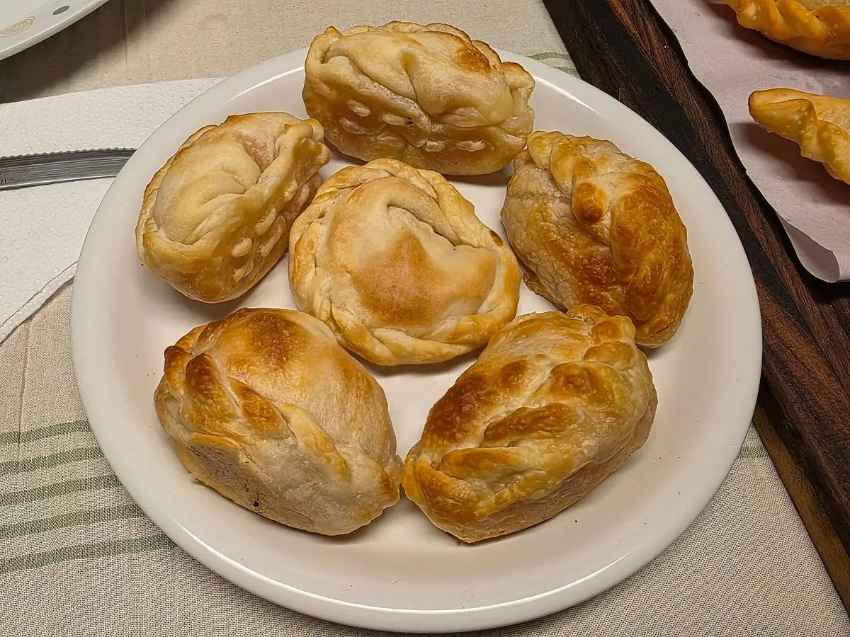 Empanadillas doradas al horno con el borde repulgado sobre un plato blanco