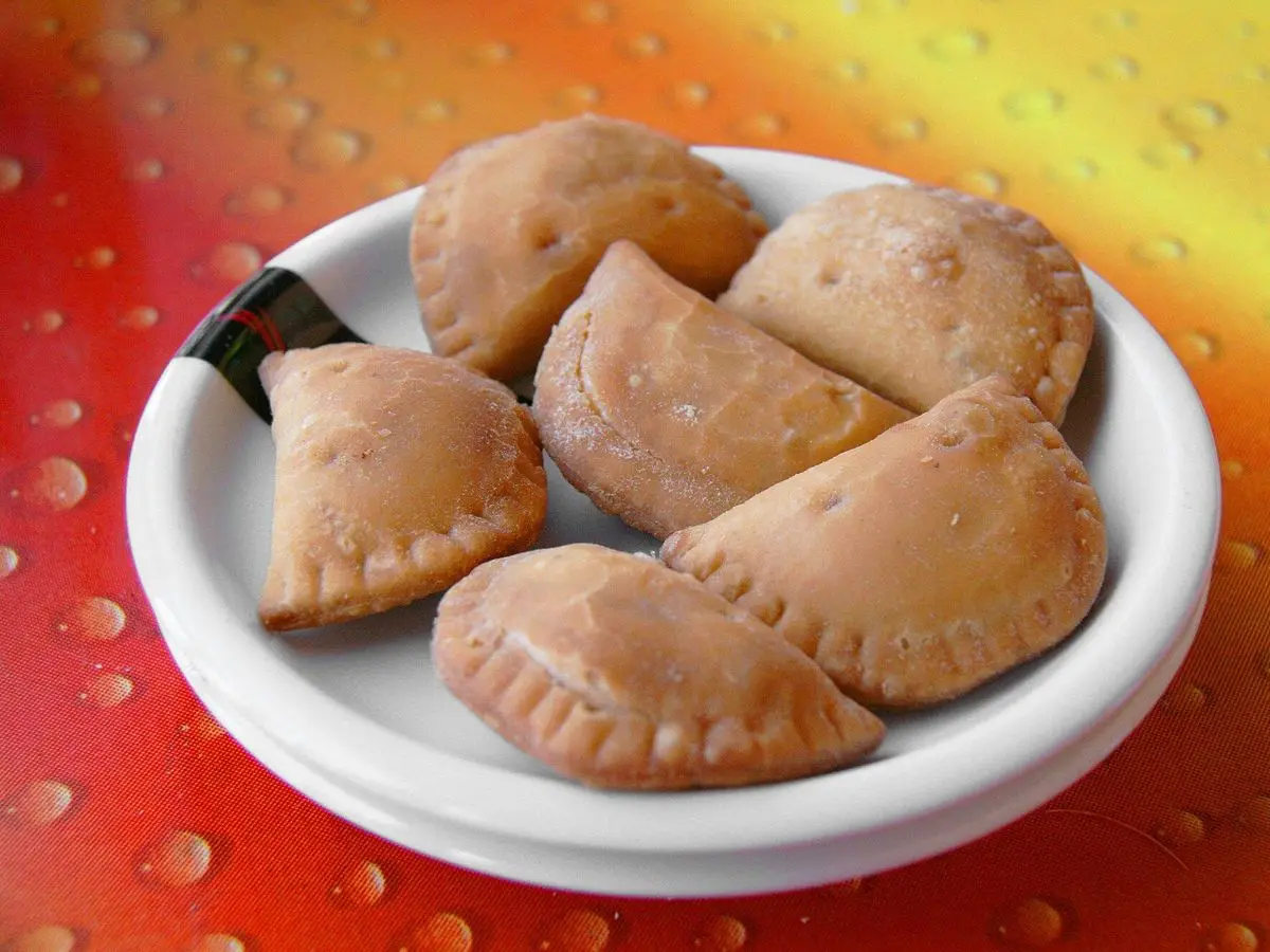 Plato blanco de empanadillas doradas rellenas de pescado sobre un mantel naranja