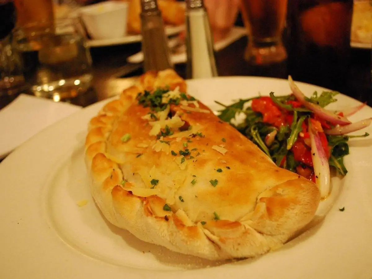 Calzone dorado relleno servido con una pequeña ensalada de tomate y hojas verdes