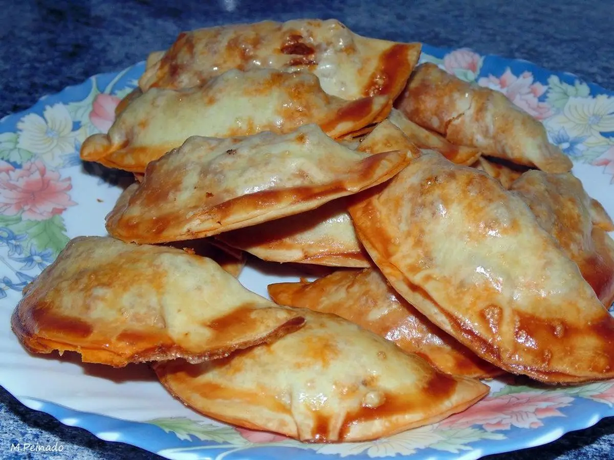 Empanadillas horneadas doradas con queso gratinado sobre un plato con flores