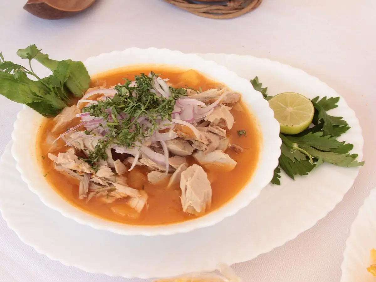 Cuenco de sopa de pescado con cebolla morada, cilantro y lima, con hojas verdes alrededor
