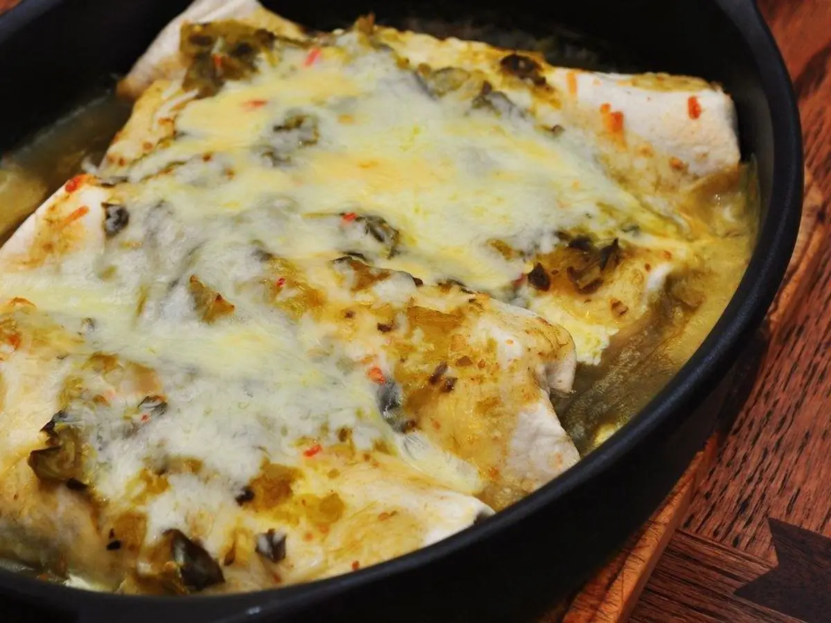 Enchiladas gratinadas con queso y salsa verde en una fuente de horno negra