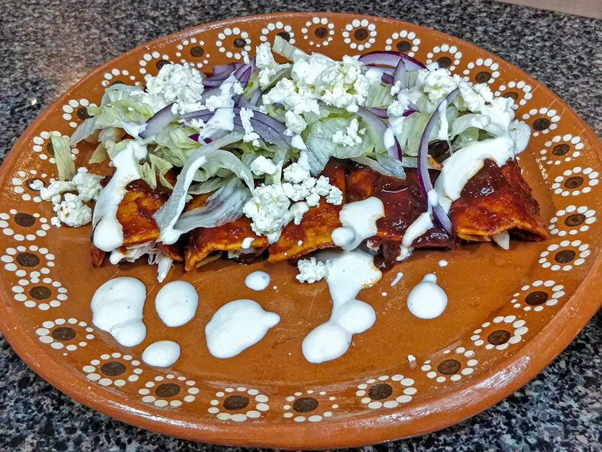 Plato de barro con enchiladas rojas cubiertas de queso, crema y cebolla morada