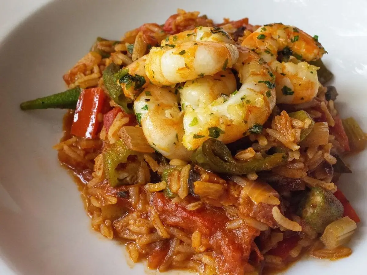 Gambas con salsa de tomate, pimiento verde y arroz en un cuenco blanco