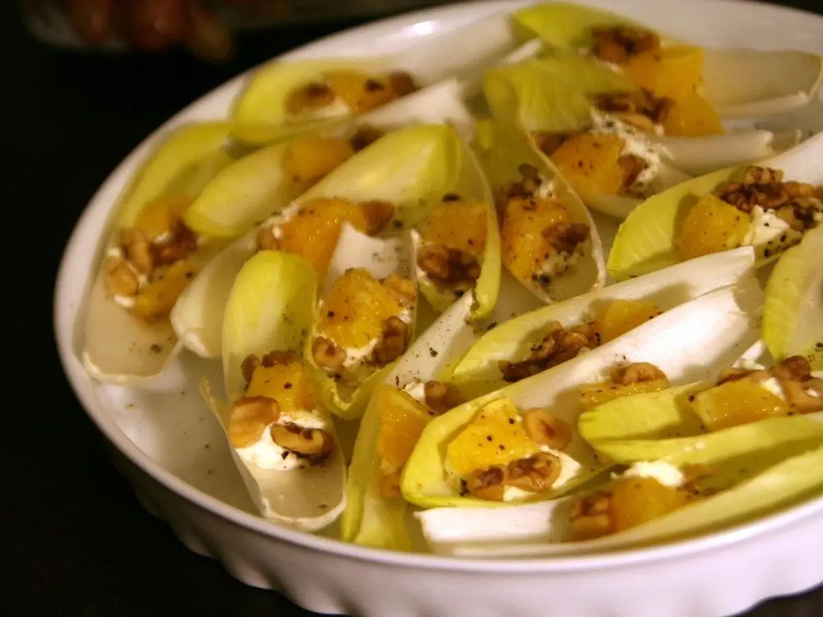 Hojas de endibia rellenas con nueces y crema sobre una fuente blanca