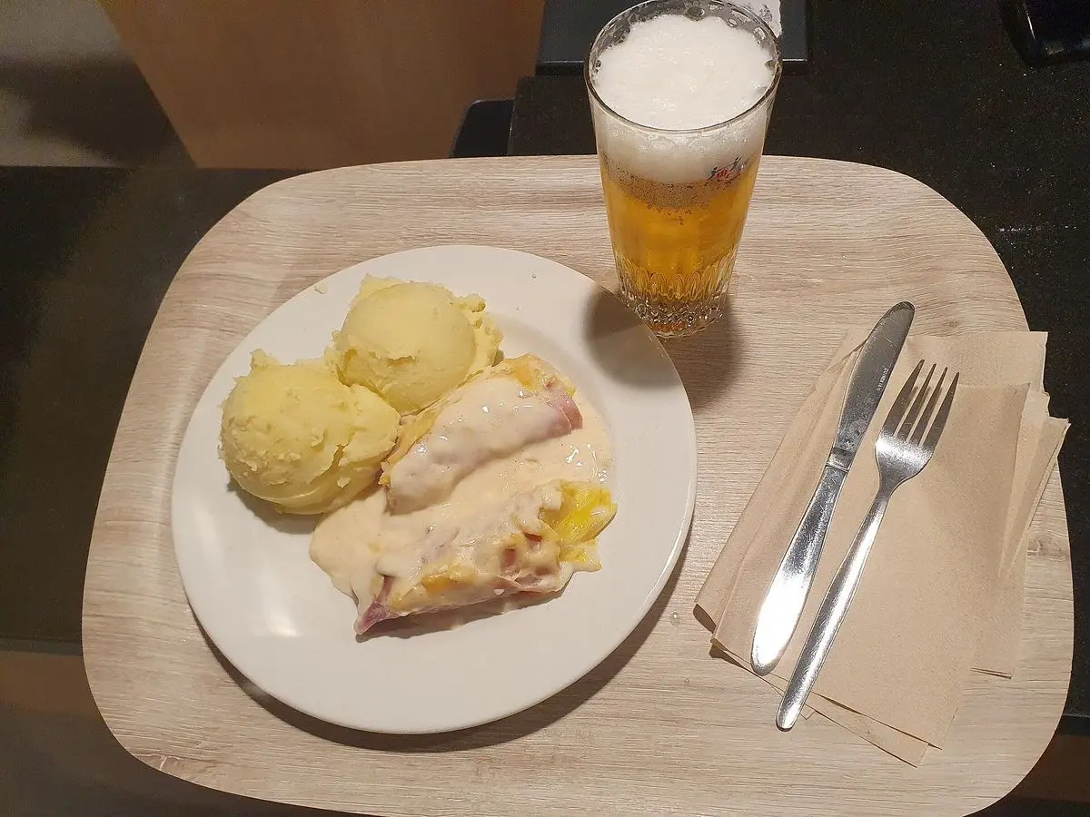 Endivias envueltas en jamón con bechamel gratinada junto a puré de patata en un plato blanco