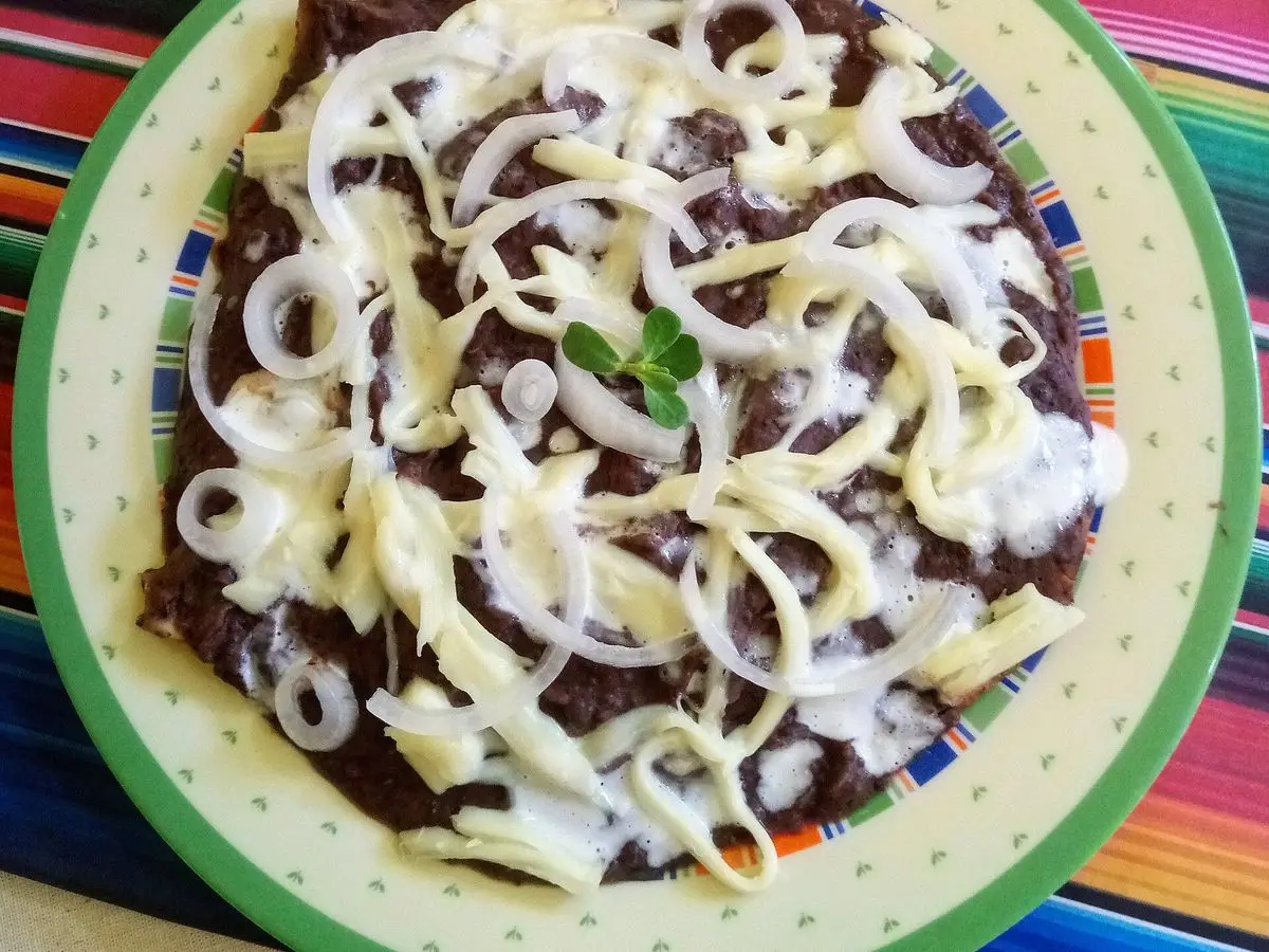 Plato de enfrijoladas cubiertas de salsa de frijol negro con queso desmenuzado y cebolla