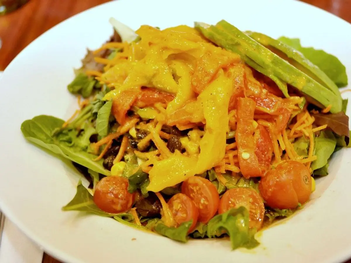 Ensalada con rúcula, tomate, pimientos asados, aguacate y queso rallado en un plato blanco