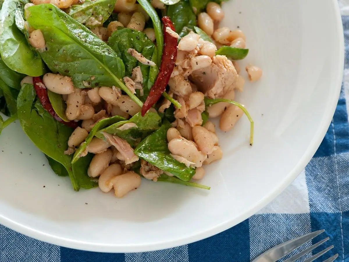 Ensalada de alubias blancas con pescado en conserva desmigado, hojas de espinaca y guindillas rojas en un plato blanco