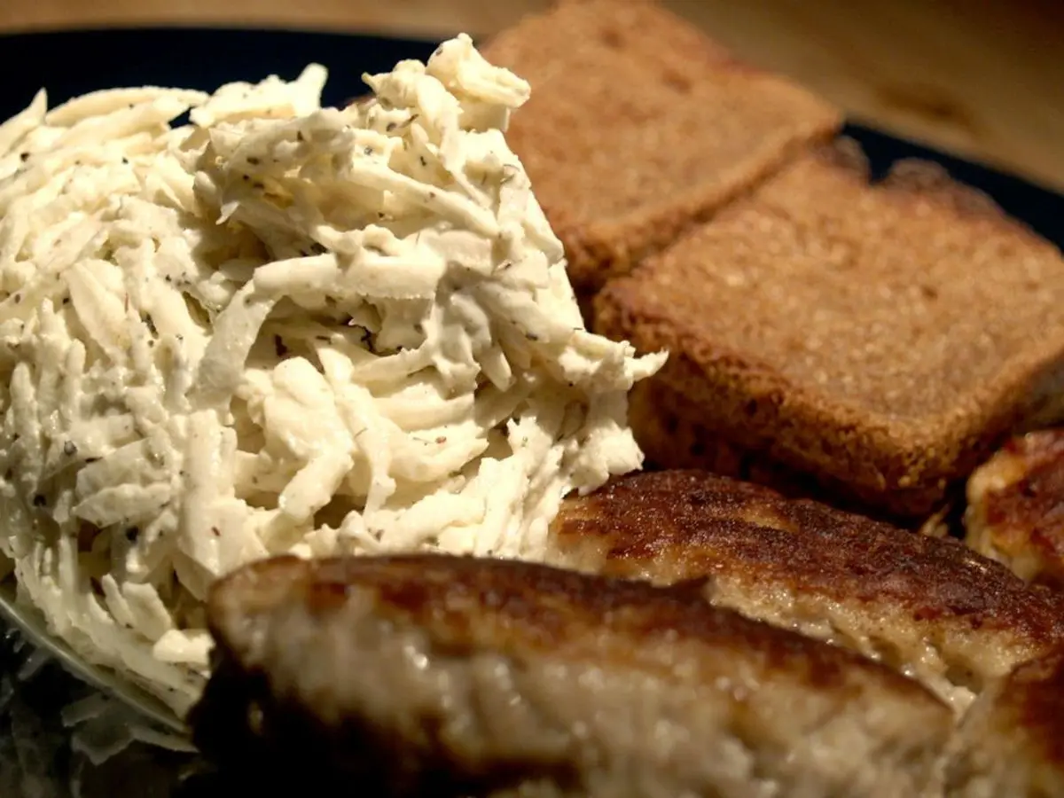 Remoulade de apionabo desmenuzado junto a pan tostado y albóndigas en un plato oscuro