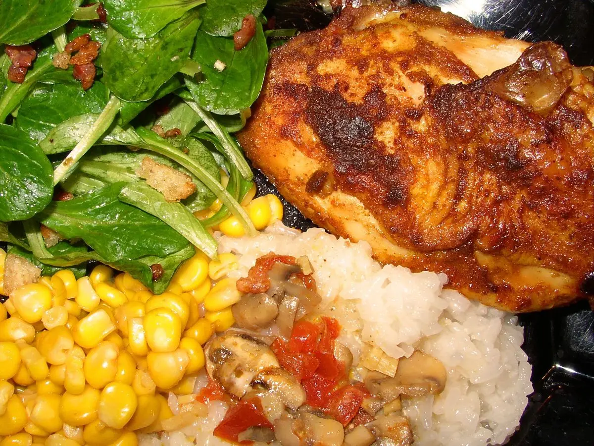 Plato con pollo a la plancha, arroz, granos de maíz y hojas de espinaca fresca