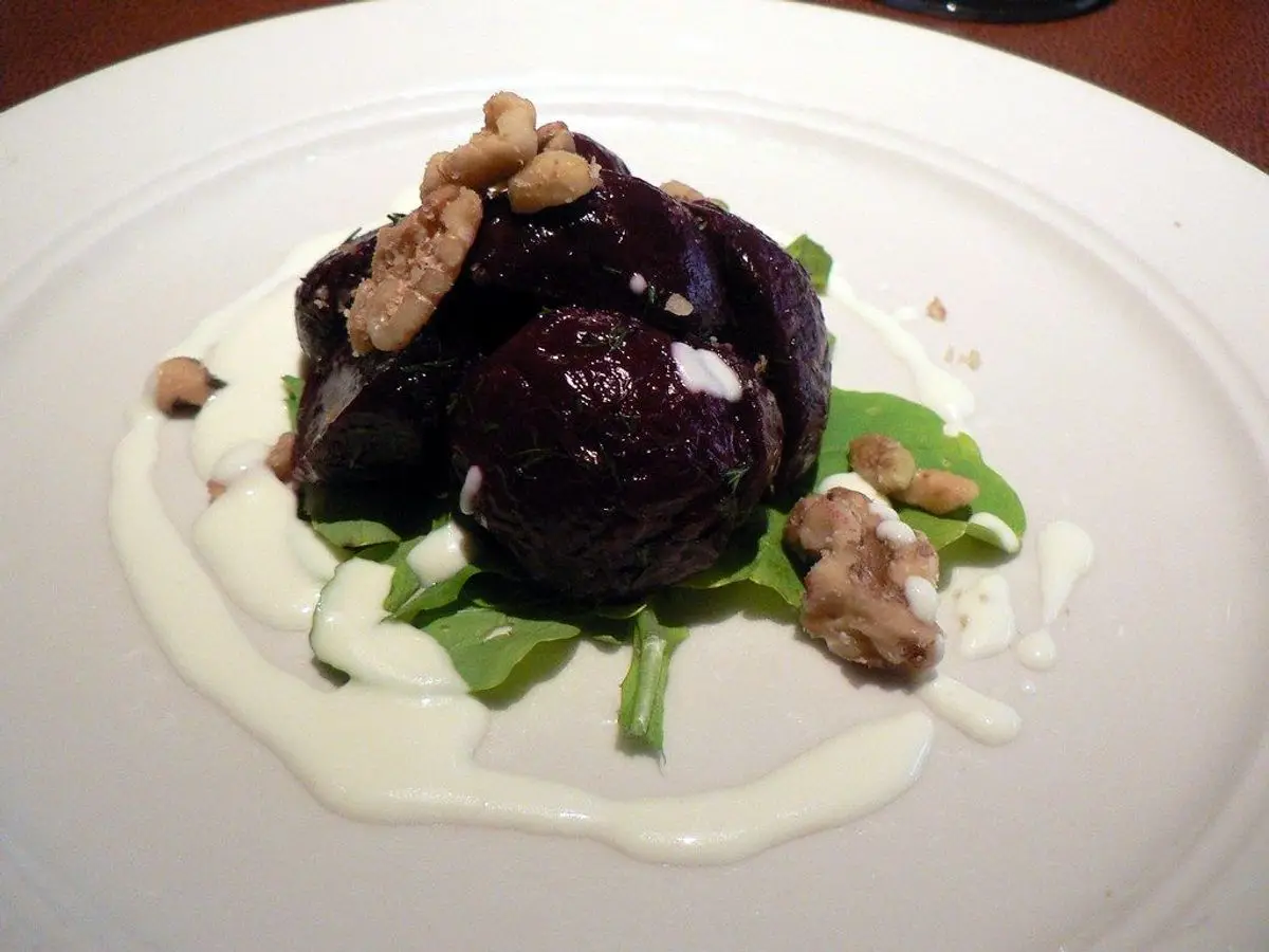 Plato blanco con remolacha asada, nueces y crema de yogur sobre hojas verdes