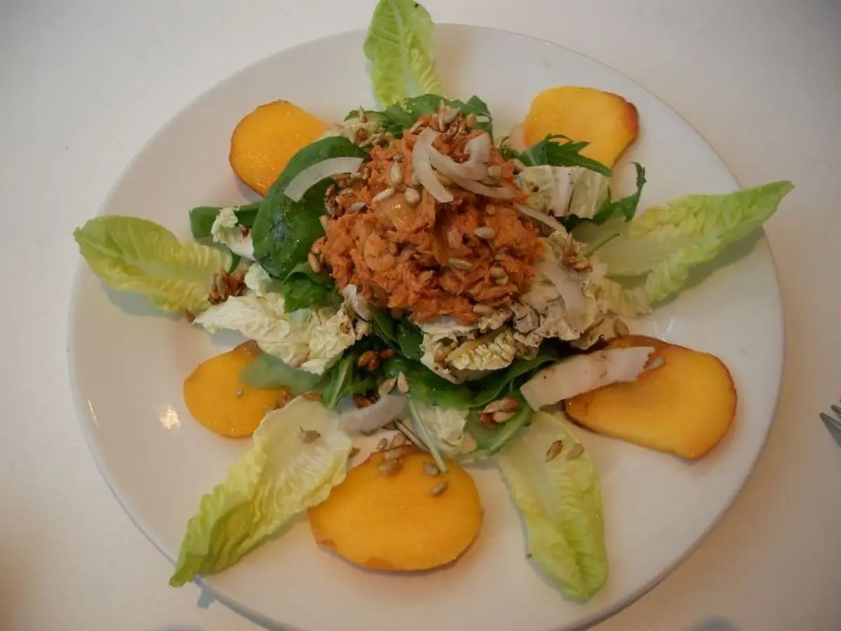 Plato blanco con ensalada de atún, rodajas de melocotón y hojas de endibia