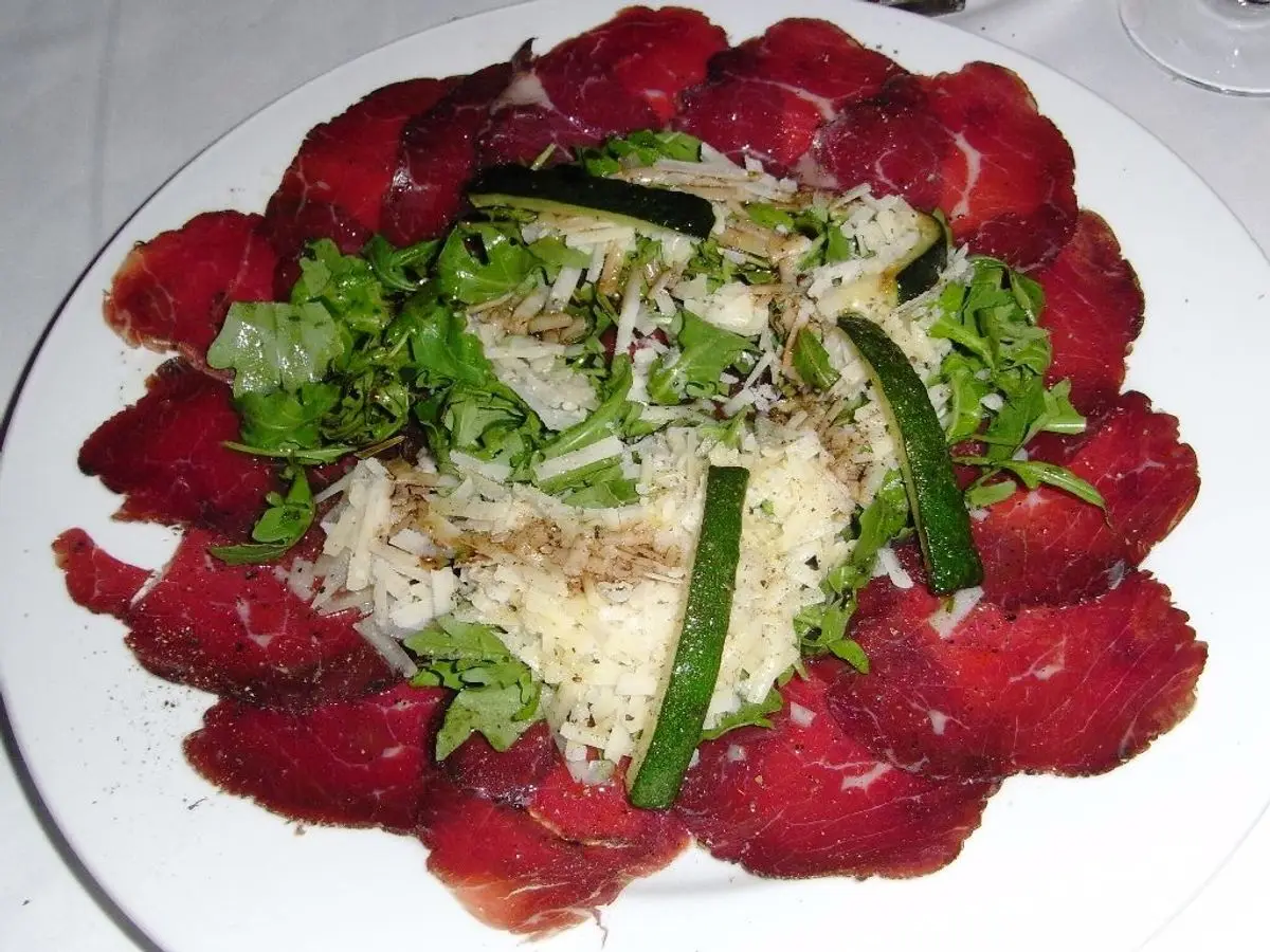 Plato de bresaola en lonchas con rúcula, pepino y lascas de queso en el centro