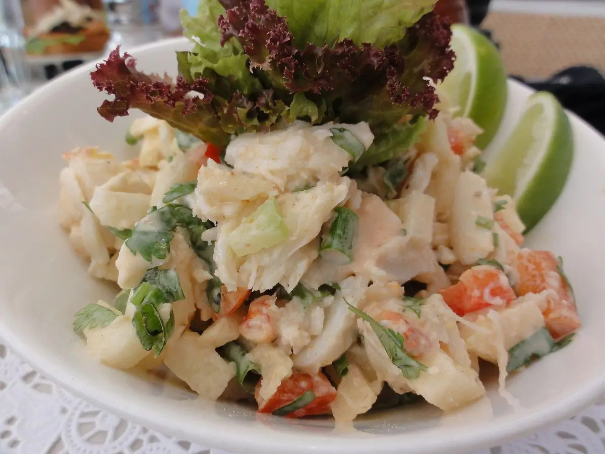 Cuenco blanco con ensalada cremosa de cangrejo, hoja de lechuga roja y gajos de lima