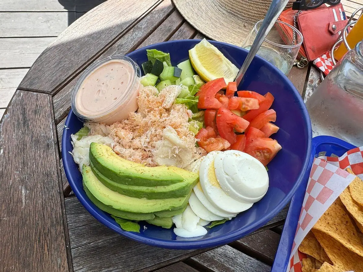 Cuenco azul con ensalada de cangrejo, tomate, aguacate y huevo duro, con un cuenquito de salsa rosa