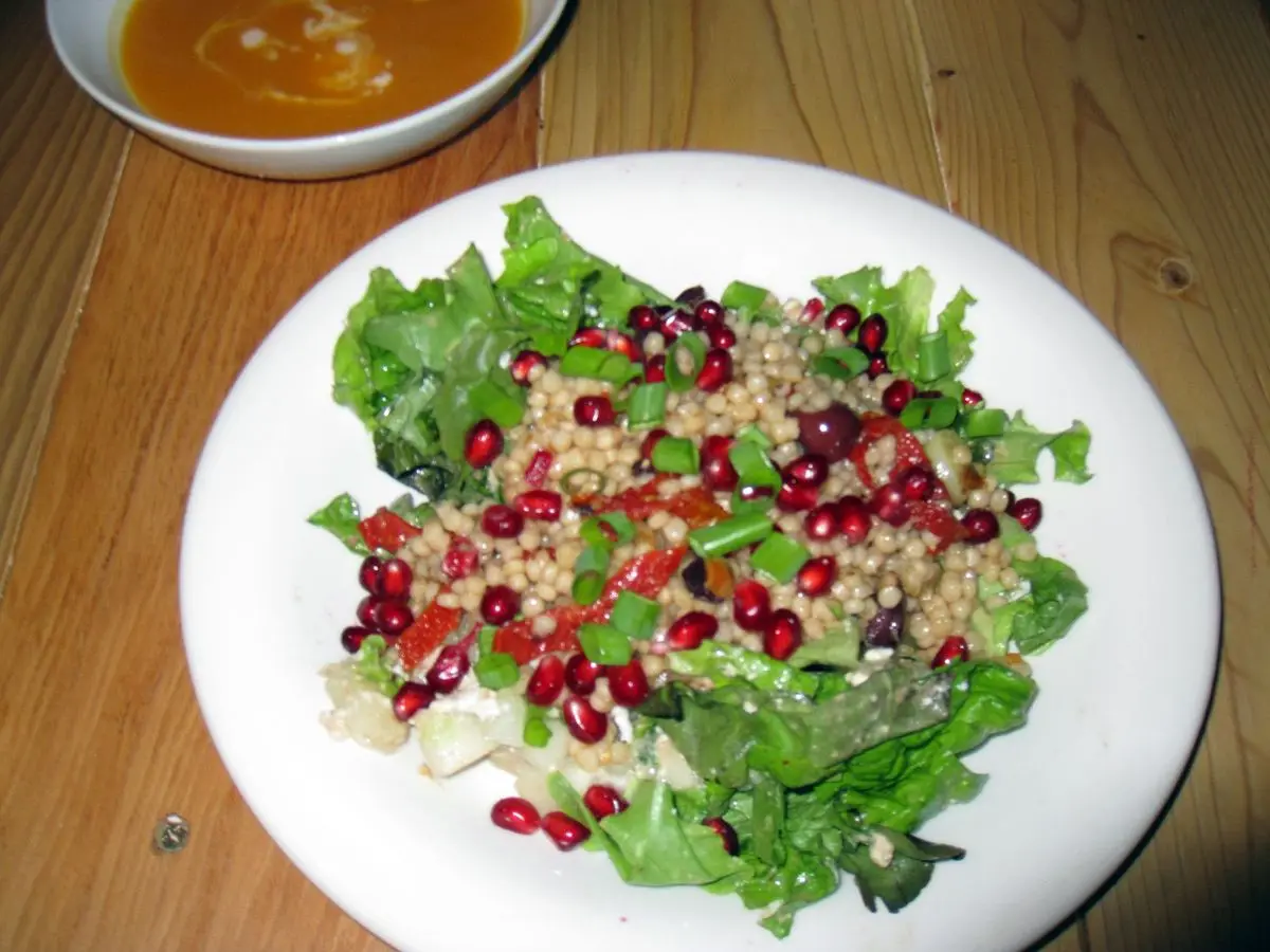 Plato blanco con ensalada de hojas verdes, cereal cocido y granos de granada