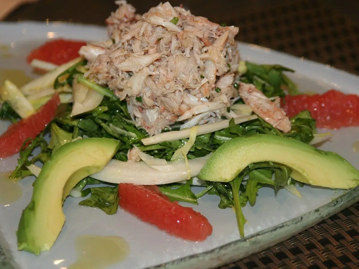 Ensalada de cangrejo desmenuzado con aguacate, gajos de pomelo y rúcula en un plato blanco