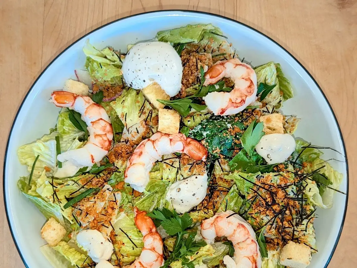 Ensalada César con langostinos cocidos, lechuga, picatostes y queso en un cuenco blanco, vista cenital