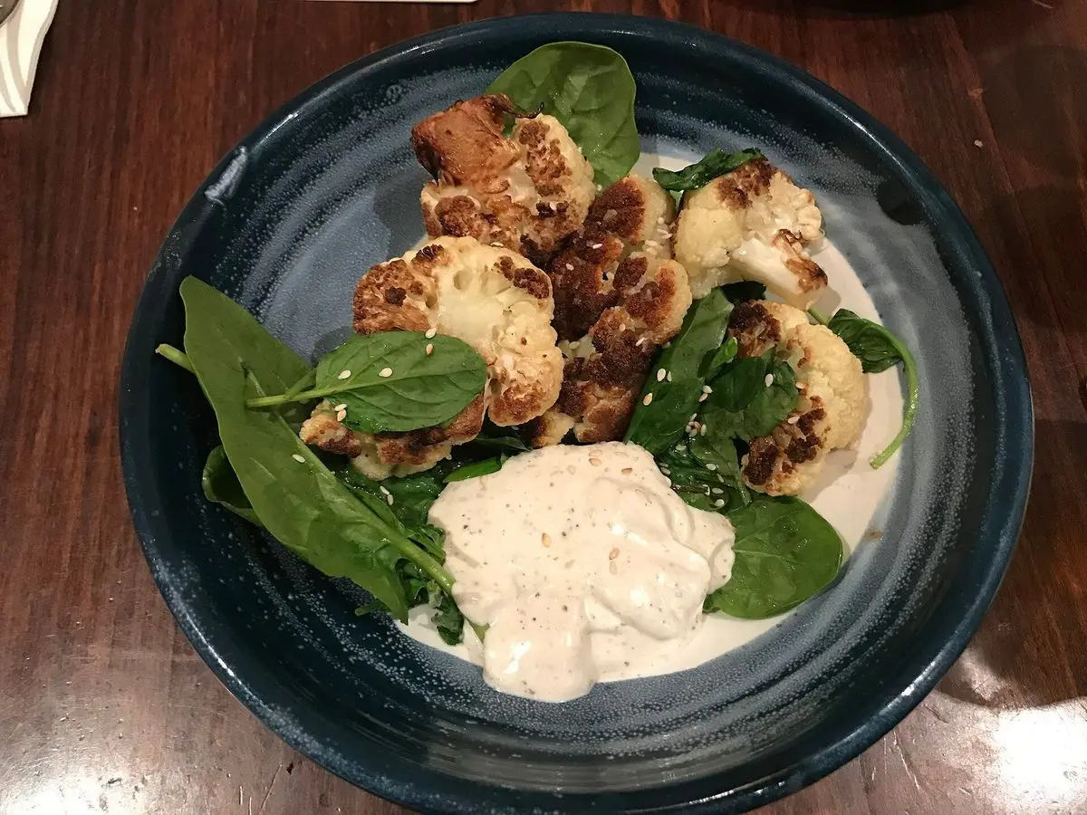 Cuenco azul con coliflor asada, espinacas frescas y salsa de yogur