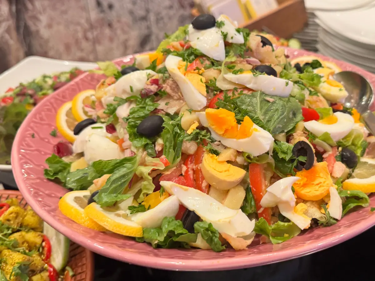 Ensalada verde con huevo cocido, aceitunas y limón en una fuente rosa