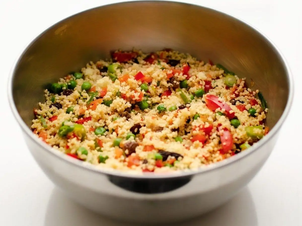 Ensalada de cuscús con pimiento rojo, guisantes, cebolleta y pasas en un bol metálico
