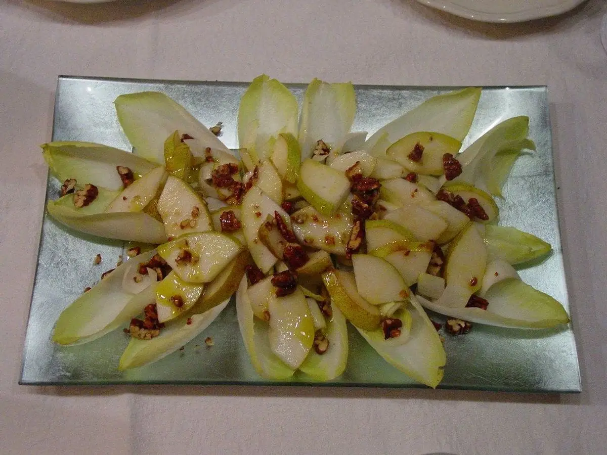 Hojas de endibia dispuestas en abanico sobre una bandeja con pera en trozos y frutos secos picados