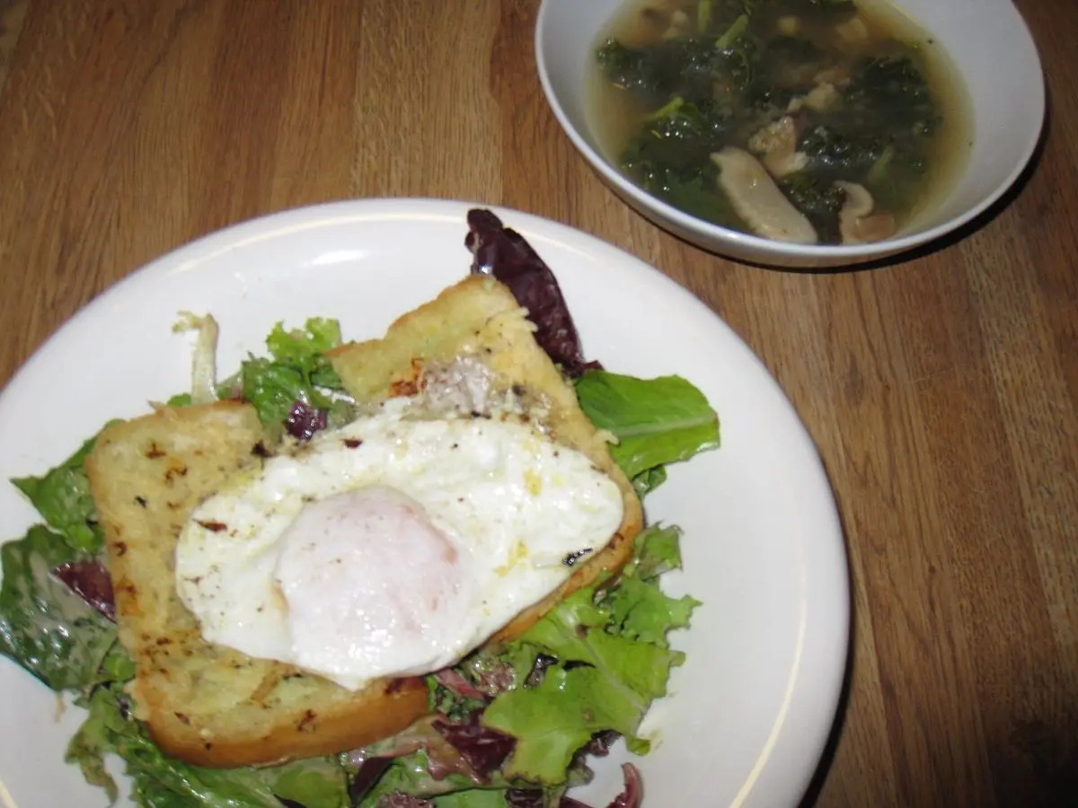 Ensalada de hojas con huevo poché sobre una tostada y un cuenco de sopa al fondo