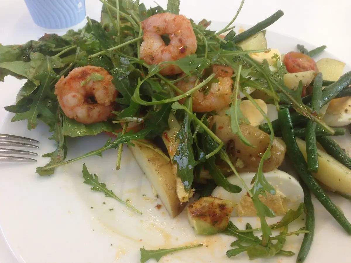 Ensalada de rúcula con langostinos, judías verdes y patata en un plato blanco