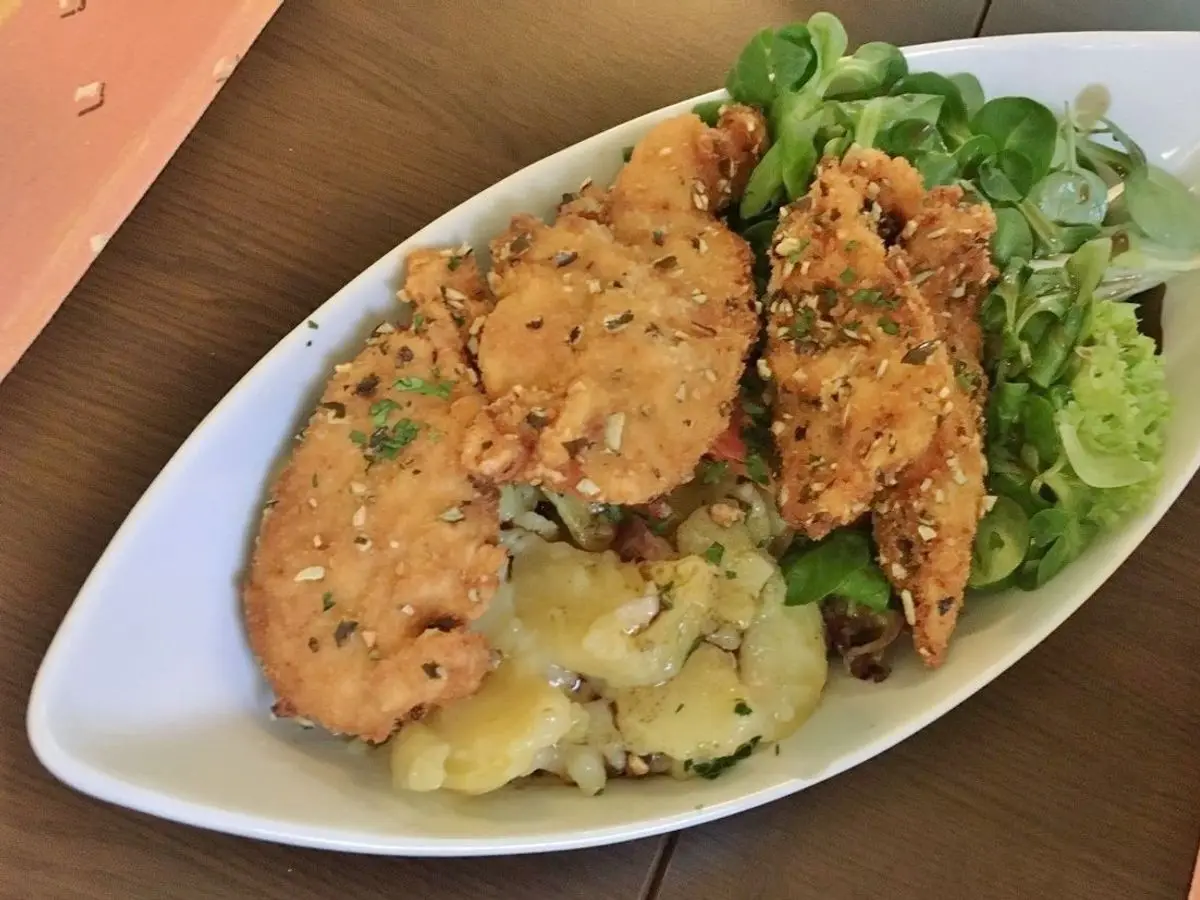 Ensalada con filetes de pollo empanado crujiente, canónigos y ensalada de patata en una fuente ovalada