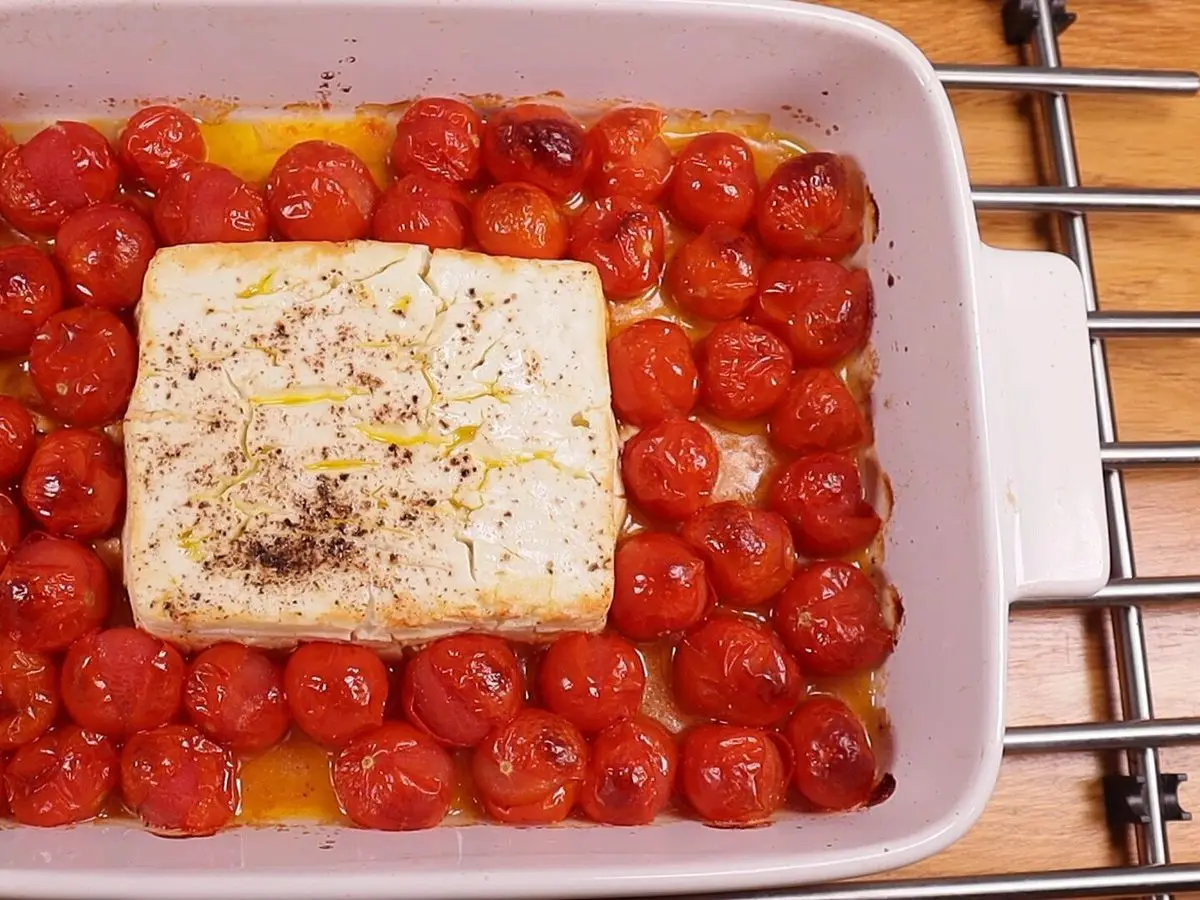 Fuente con bloque de queso feta horneado rodeado de tomates cherry asados