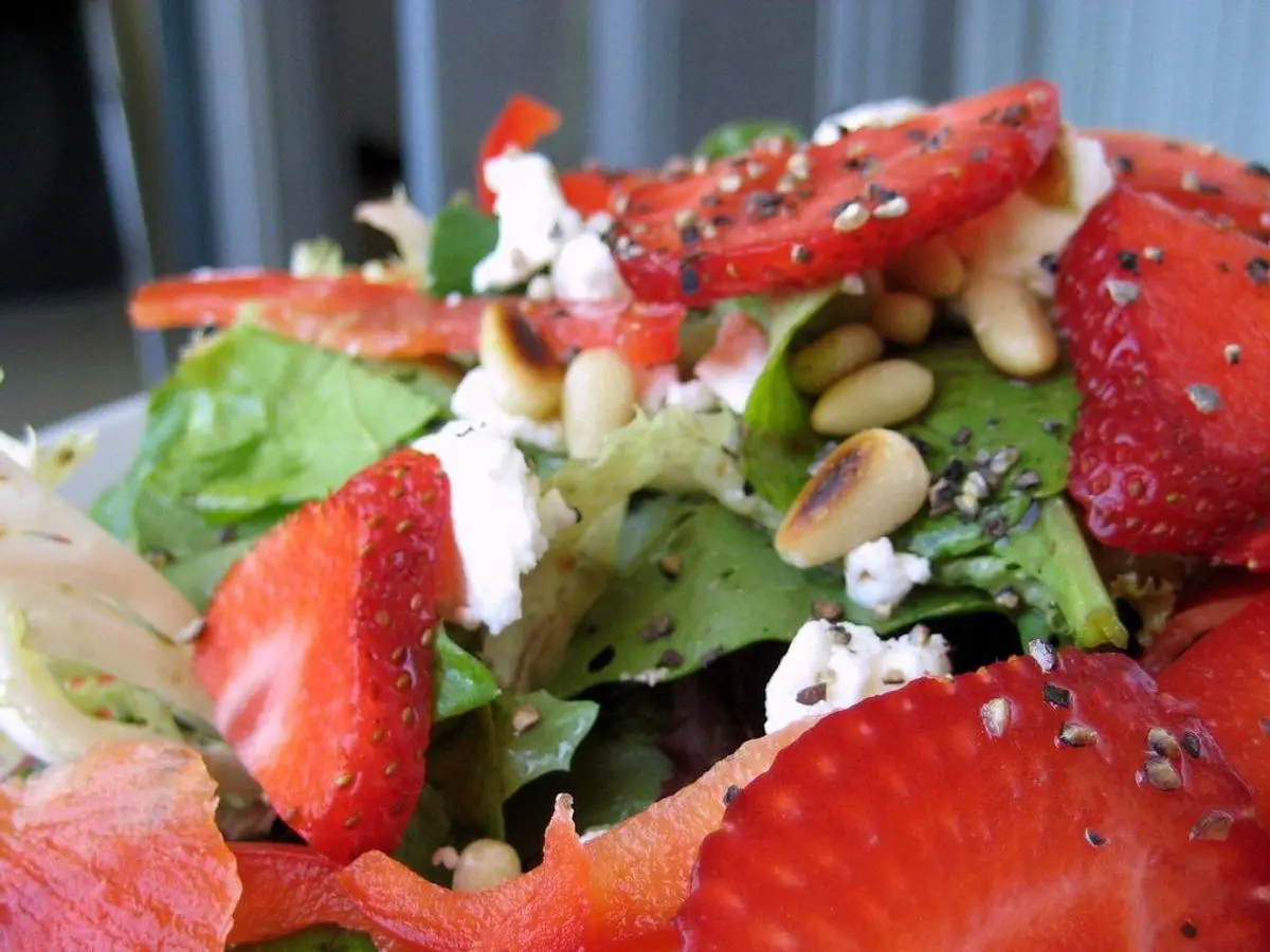 Ensalada de espinacas con fresas en rodajas, queso desmenuzado y piñones