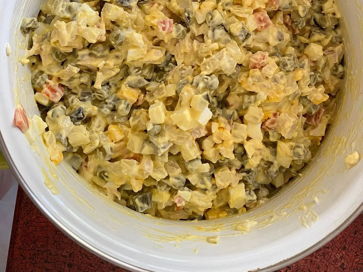 Cuenco blanco lleno de ensalada de pollo con patata cocida, huevo, pepinillo y mayonesa