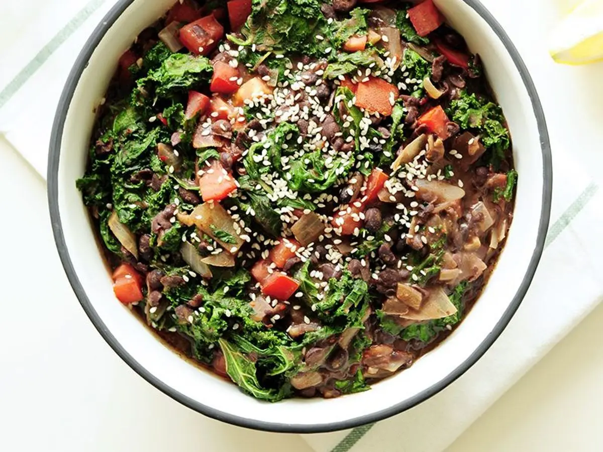 Cuenco blanco de ensalada tibia de alubias negras con kale y tomate
