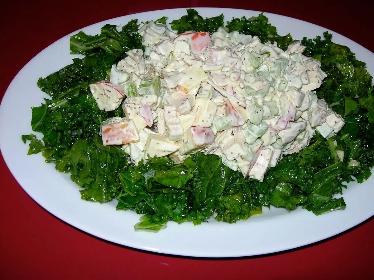 Ensalada cremosa con trozos de pollo sobre una cama de kale en un plato ovalado blanco