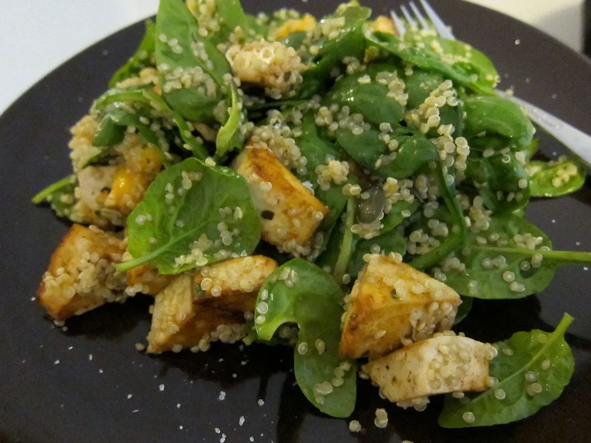 Plato negro con espinacas frescas, quinoa y dados de pan o tofu dorados