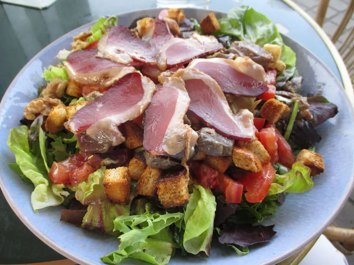 Ensalada con lonchas de magret de pato ahumado, picatostes, tomate y lechuga en un plato azul