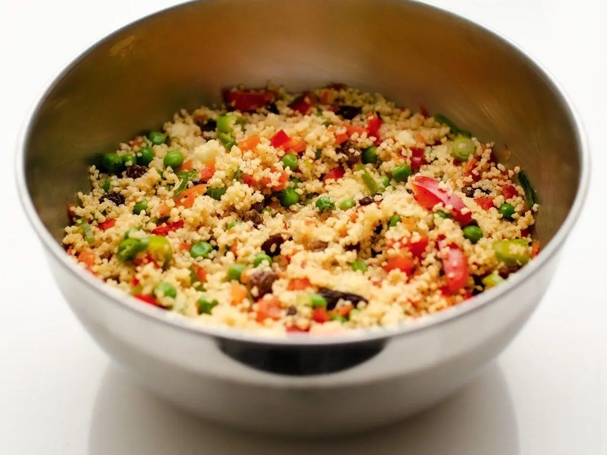 Cuenco metálico de ensalada de cuscús con pimiento rojo, guisantes y verduras picadas