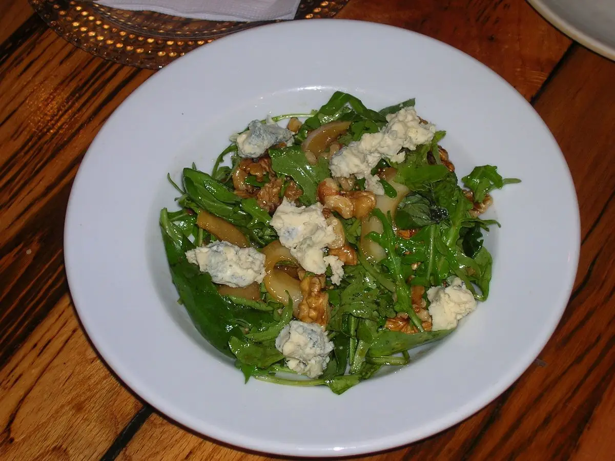 Plato blanco con hojas verdes, queso azul desmenuzado y nueces