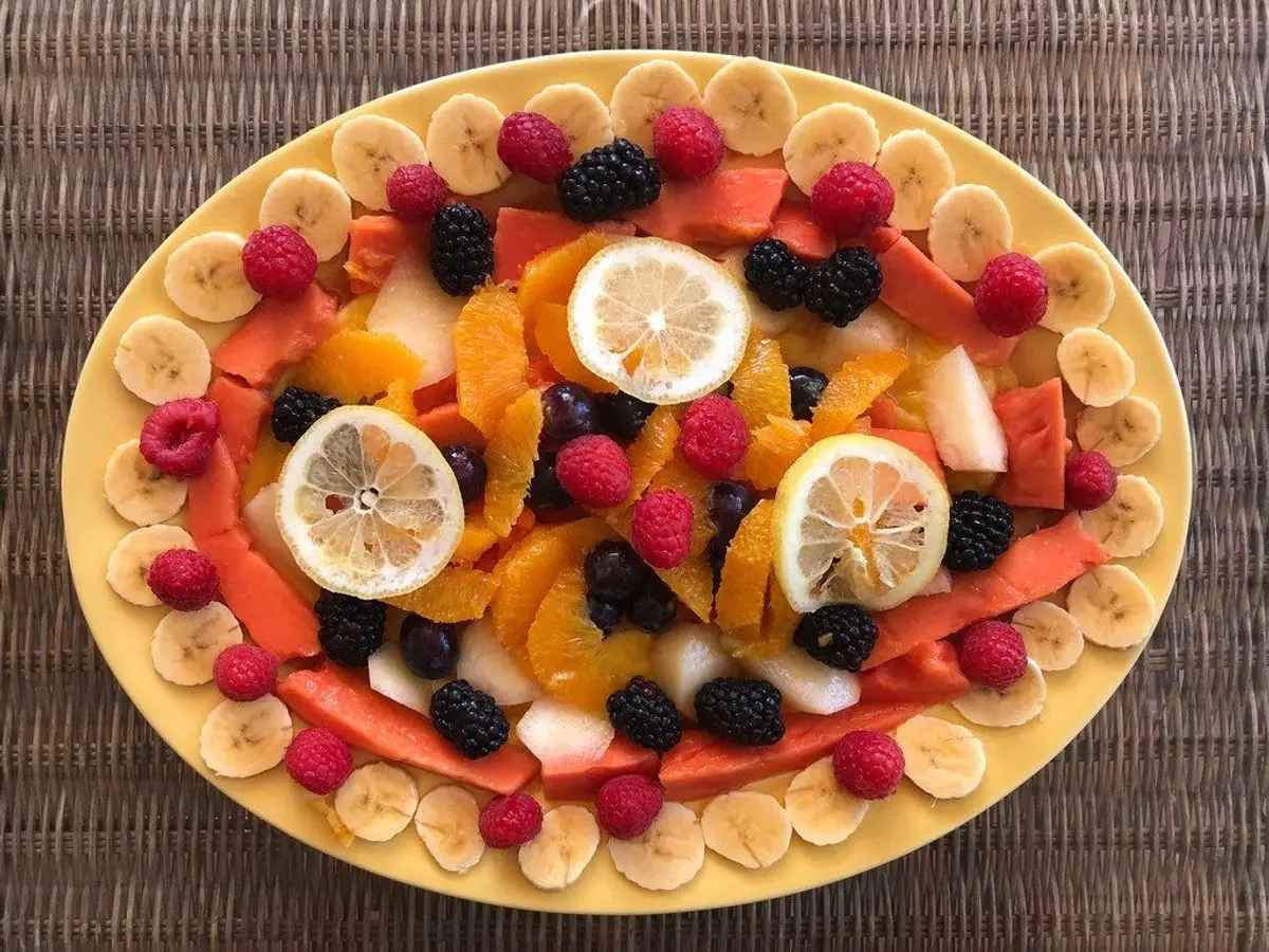 Fuente ovalada con ensalada de frutas exóticas: rodajas de cítricos, frambuesas, moras y plátano